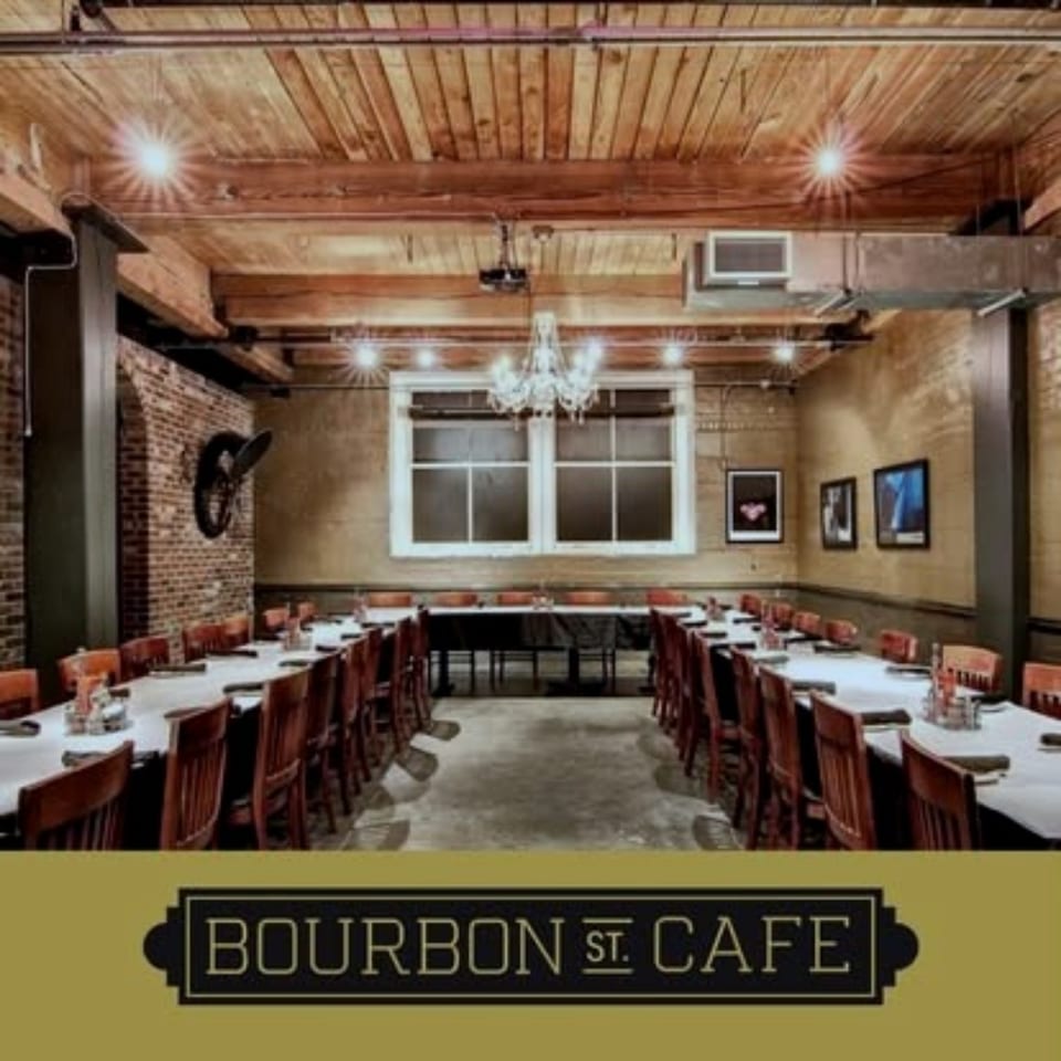 Bourbon Street Cafe dining room with exposed brick walls, wood-beamed ceiling, chandelier, framed artwork, and white-clothed tables.