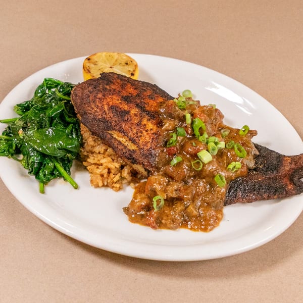 Blackened fish with rice, sauce, spinach, and a lemon wedge on a white plate.