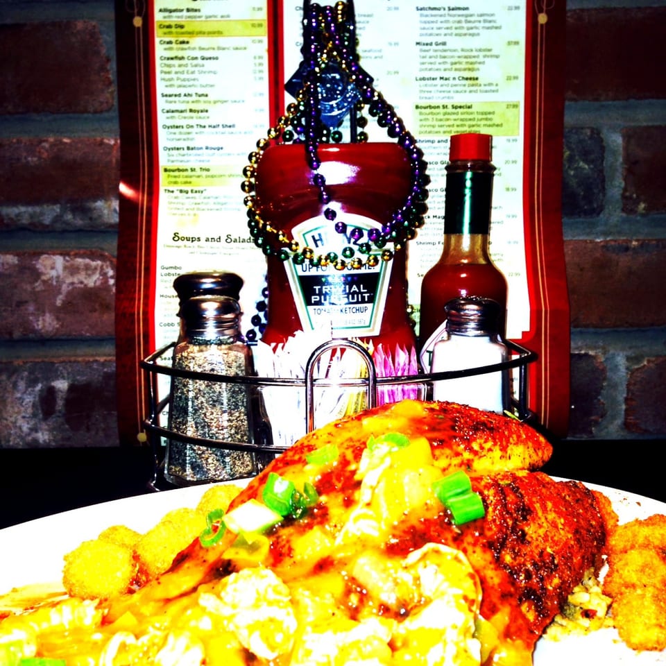 Cheesy, seasoned fries topped with green onions beside restaurant condiments, a menu, and festive beads.