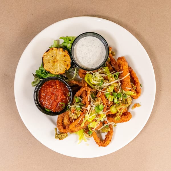 Crispy fried calamari with grilled lemon, marinara, and ranch dressing on a white plate.