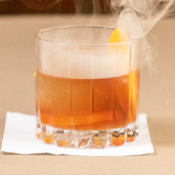 Smoked cocktail with an orange peel garnish in a rocks glass on a white napkin.