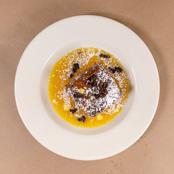 Bourbon St. Cafe's bread pudding with golden sauce, raisins, and powdered sugar on a white plate.