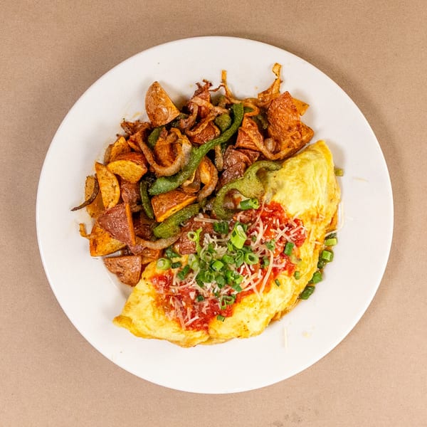 Omelet topped with red sauce, cheese, and green onions, served with roasted potatoes and peppers.