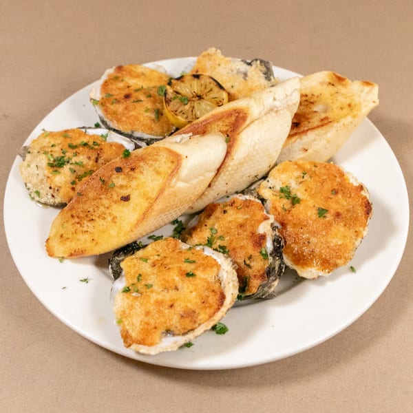 Baked oysters topped with golden breading and parsley, served with toasted bread and a lemon wedge.
