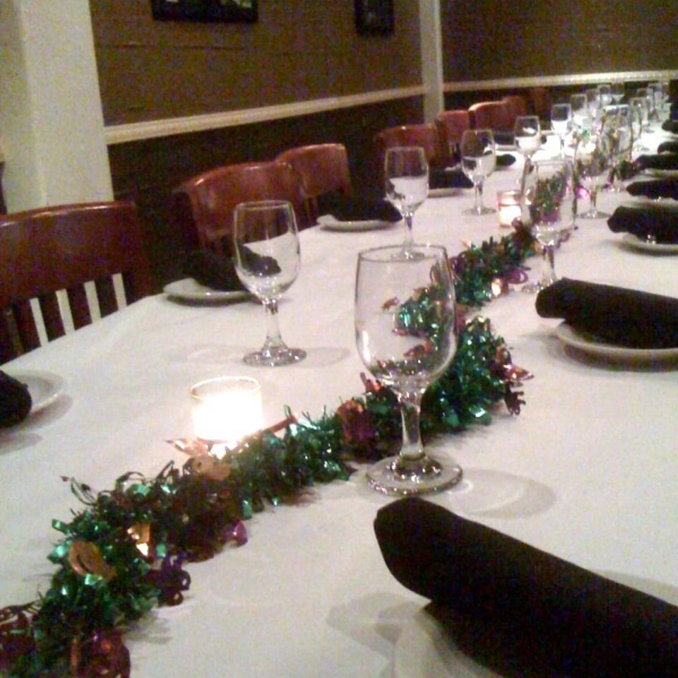 Festively decorated restaurant table with white linens, wine glasses, plates, dark napkins, and a glowing candle.