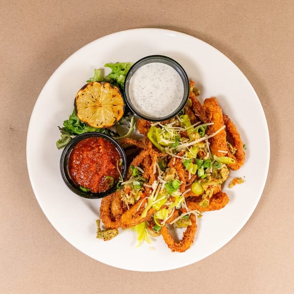 Fried calamari with two dipping sauces, grilled lemon, and greens on a white plate.