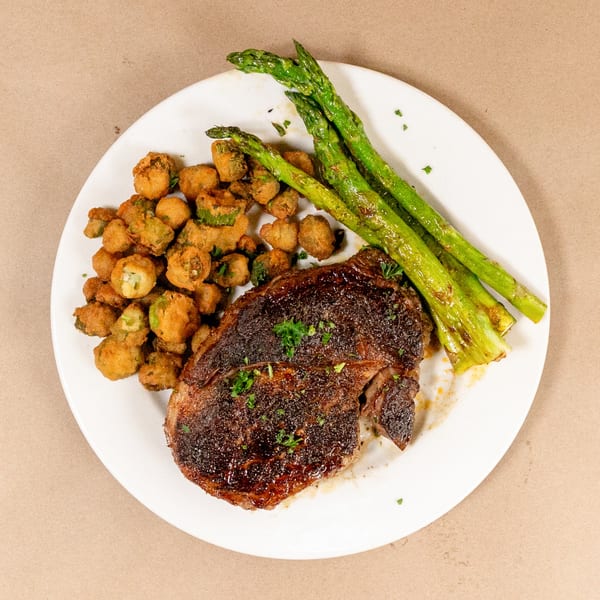Bourbon St. Cafe's steak with fried okra and asparagus on a white plate.