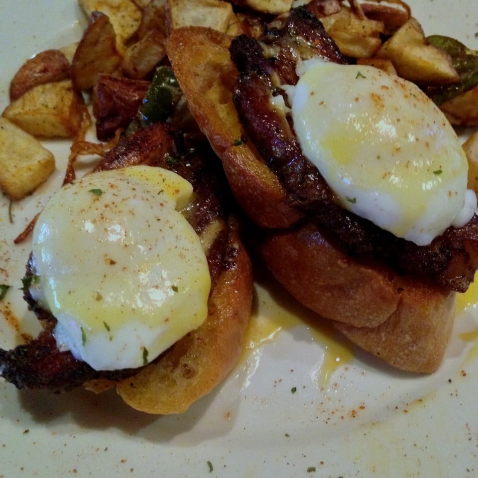 Hearty plate of roasted potatoes, grilled sausage, and two fried eggs sprinkled with herbs.