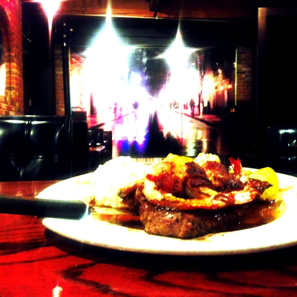 Plate of grilled meat, roasted vegetables, and potatoes on a restaurant table in a dimly lit dining room.