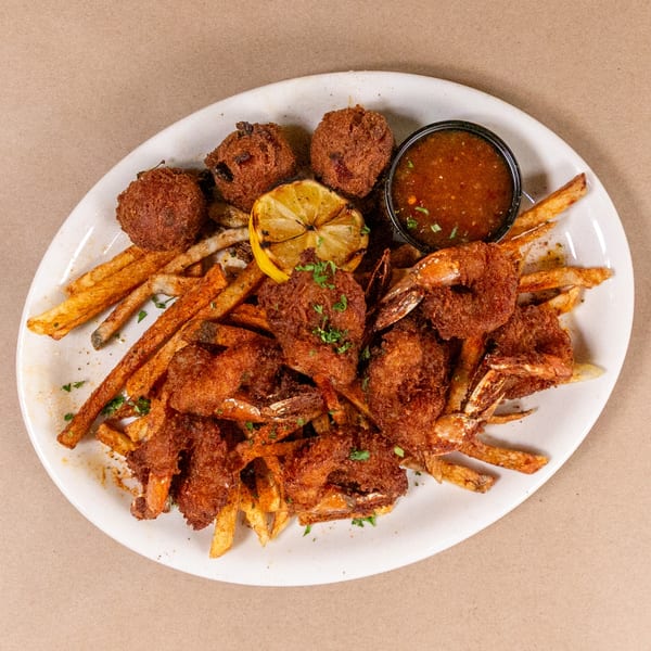 Fried shrimp and hushpuppies with french fries, a grilled lemon, and dipping sauce on a white plate.