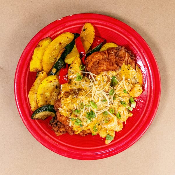 Bourbon St. Cafe's fried chicken with creamy pasta, shredded cheese, and roasted vegetables on a red plate.
