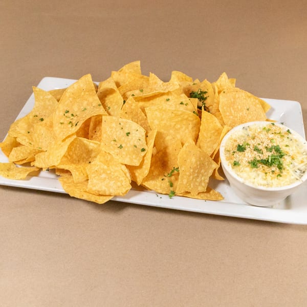 A white rectangular plate holds a pile of tortilla chips and a small bowl of cheesy dip.