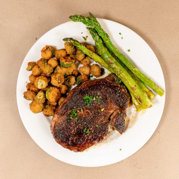 Bourbon St. Cafe's steak with fried okra and asparagus on a white plate.