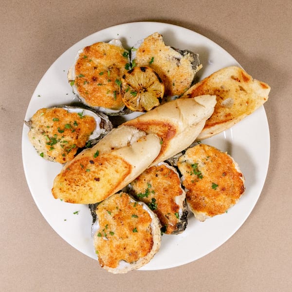 A white plate holds baked oysters, grilled lemon, and toasted bread, garnished with parsley.