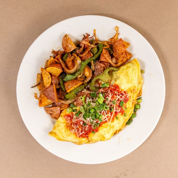 A Bourbon St. Cafe omelet with red sauce, cheese, and green onions, served with roasted potatoes and peppers.