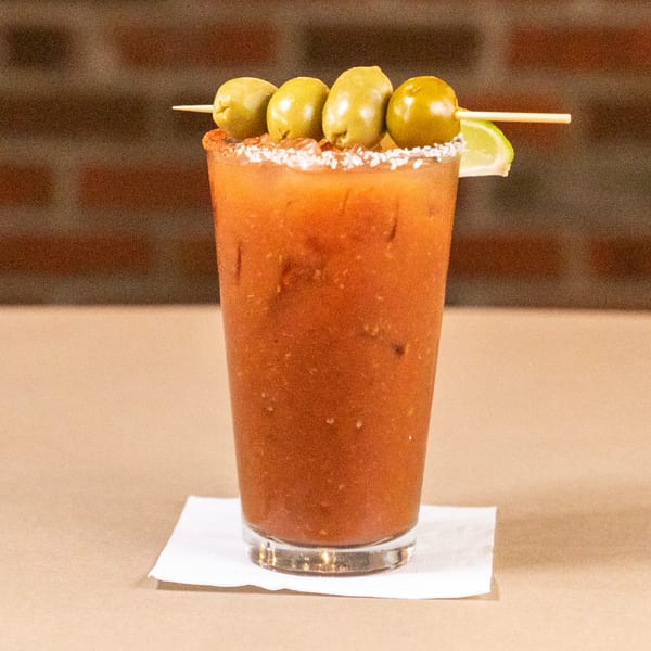 A Bourbon St. Cafe Bloody Mary cocktail garnished with olives and a lime wedge.