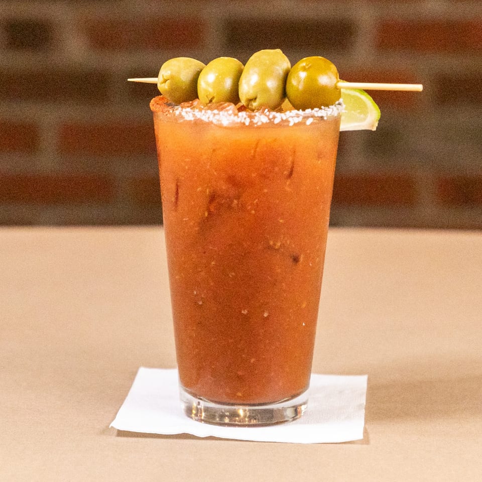 A Bourbon St. Cafe Bloody Mary cocktail garnished with olives and a lime wedge.