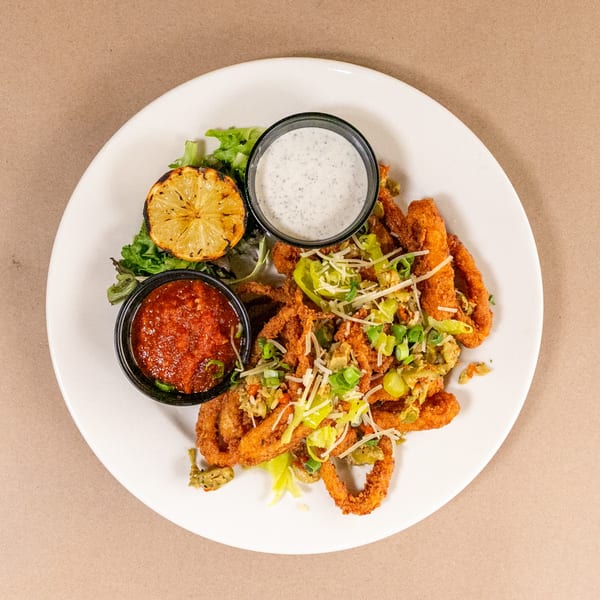 Fried calamari with two dipping sauces, grilled lemon, and greens on a white plate.