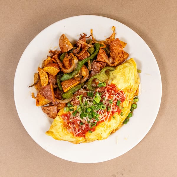 A Bourbon St. Cafe breakfast plate with a folded omelet topped with salsa, cheese, and scallions, alongside roasted potatoes, peppers, and onions.